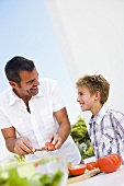 Father and son preparing salad out of doors