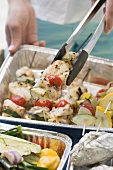 Woman holding fish and vegetable kebab in barbecue tongs