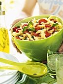 Person holding large bowl of pasta salad with tomatoes