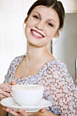 Young woman holding a cup of coffee with frothy milk