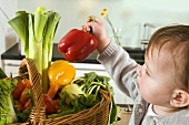 Toddler taking a red pepper out of a basket of vegetables
