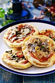 Four small pizzas topped with tomatoes, capers, olives & cheese