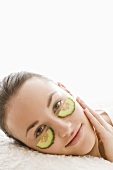 Young woman with cucumber slices under her eyes