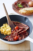 Scrambled egg with bacon and cherry tomatoes in frying pan