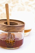 Honey dipper in honey jar in front of glass of milk