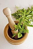 A wooden mortar and pestle with fresh basil