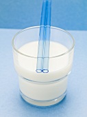 Blaue Strohhalme auf Glas Milch