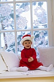 Kleines Mädchen im Nikolauskleid sitzt vor dem Fenster