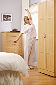 Woman in pyjamas yawning and stretching in bedroom