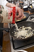 Reis und Zwiebeln für Risotto in einer Pfanne anschwitzen
