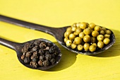 Green and black peppercorns on wooden spoons