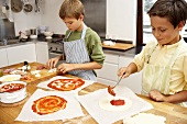 Two boys putting toppings on pizzas