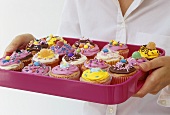 Frau hält pinkfarbenes Tablett mit Cupcakes