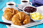 Croissants, butter, strawberry jam and two cups of coffee