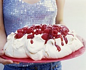 Hands holding a raspberry pavlova