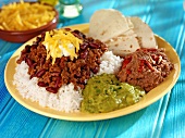 Chili con carne on rice with tortilla and two sauces