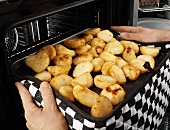 Man taking roast potatoes out of the oven