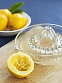 Ausgepresste Zitronenhälfte mit Zitronenpresse und -saft