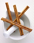Four cinnamon sticks in a mortar with pestle
