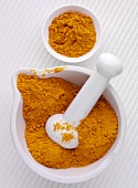 Ground turmeric in a mortar with pestle and a small dish