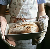 Child holding freshly baked bread in baking tin