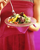 A woman holding a plate of rocket and vegetable salad