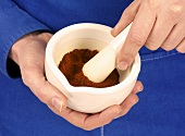Hands holding mortar containing chilli powder