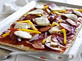 Unbaked pizza topped with pepperoni, yellow pepper & mozzarella