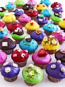Many muffins with coloured icing and decorations