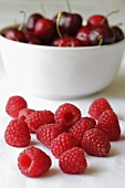 Fresh raspberries in front of a bowl of cherries