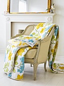Flowery bedspread and cushion on upholstered chair by fireplace