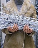 Frau hält weiße Zweige (Weihnachtsdeko) vor dem Haus