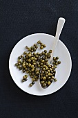 Green peppercorns on plate and spoon