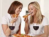 Two happy women eating pizza