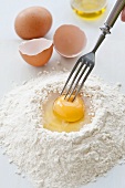 Hand pricking an eggs yolk on a mound of flour with a fork