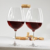 Two glasses of red wine with a cork balanced between them