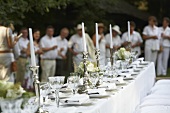 Hochzeitstafel in Weiß, im Hintergrund Hochzeitsgäste
