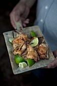 A man serving barbecued spring chicken with limes