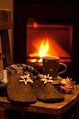 Filzpantoffeln, Lebkuchen und Kakao auf Stuhl vor Kaminfeuer