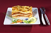 A slice of lasagne with a side salad and lemon