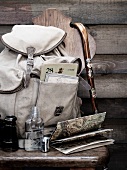 Rucksack mit Spazierstock, Fernglas, Flachmann und Karten auf Holzstuhl