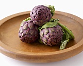 Three artichokes on a wooden plate