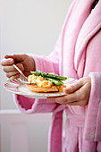 A woman in a dressing gown hold a plate of scrambled eggs and asparagus