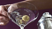 Stirring Martini with olive on cocktail stick