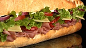 A sub sandwich filled with ham, cheese, lettuce and tomato