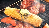 Corn on the cob with herb butter, peppers and pork steaks on the barbecue