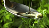 Olivenöl fliesst über Löffel