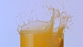 Orangenschnitz fällt in ein Glas Orangensaft