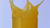Eiswürfel fällt in ein Glas Orangensaft