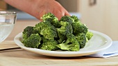 A hand taking a plate of broccoli florets